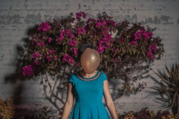 This image is a woman in a blue dress with her face hidden behind a balloon.