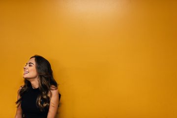 photo-woman-of-color-leaning-on-mustard-yellow-wall-happy-smiling