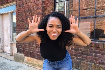 curly hair woman smiling in front of a brick wall