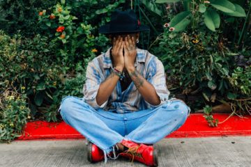 man sitting with his face covered and legs crossed