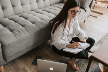 woman sitting on floor writing in notebook with computer